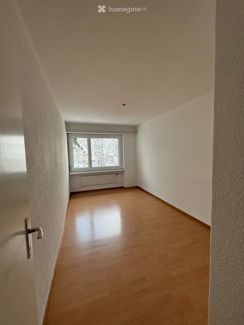 Empty hallway with wooden floor and a window on the right side, white walls, door on the left.