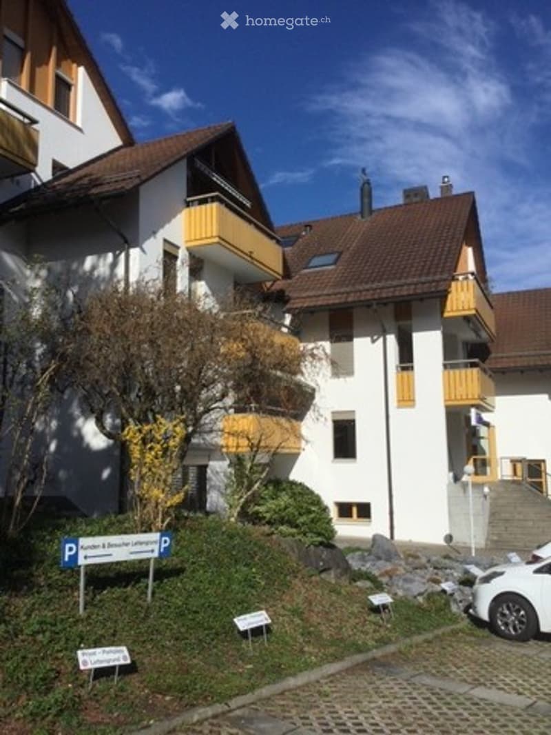 Multi-story residential building with white facade, brown roof, and yellow balconies. A parking sign is visible in the foreground.