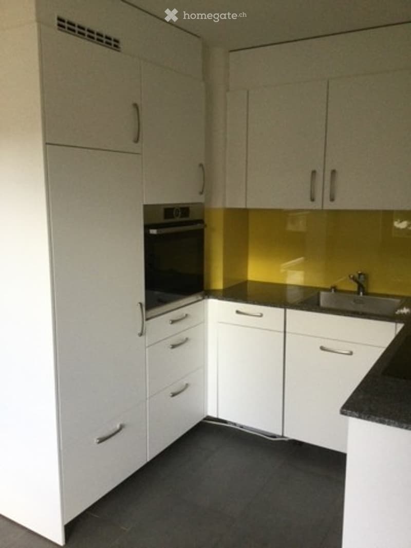 Modern kitchen with white cabinets, black countertops, and a built-in oven. Features a sleek design with a yellow backsplash.