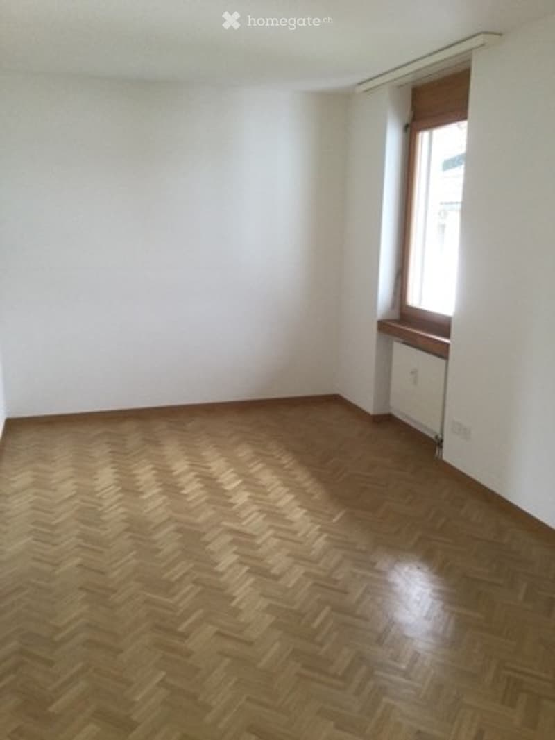 Empty room with wooden herringbone flooring, white walls, and a single window with a small wooden sill.