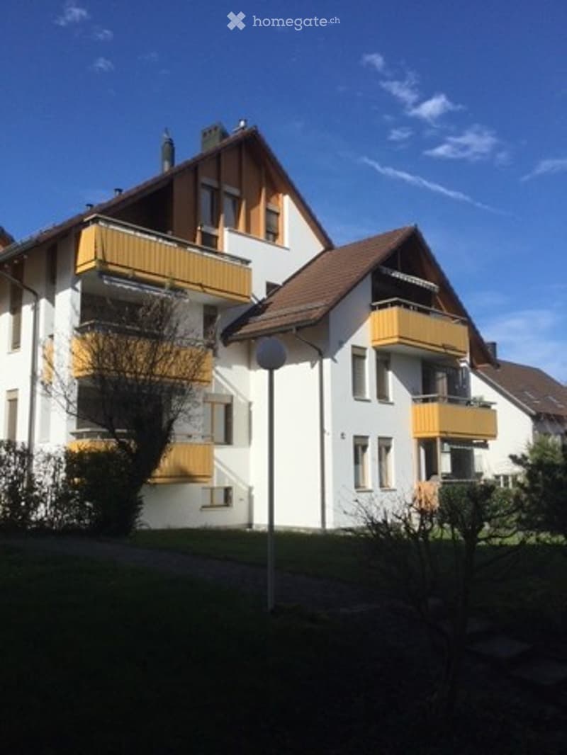 Multi-story residential building with white walls, yellow balconies, and a brown roof under a clear blue sky.