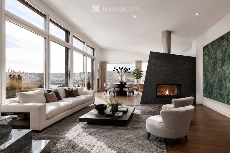 Modern living room with large windows offering a scenic view, a white sectional sofa, a black coffee table, a fireplace, and a dining area with a round table and chairs.