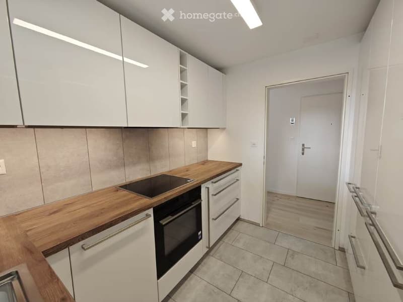 Modern kitchen with white cabinets, wooden countertop, built-in oven, and white tiled floor.