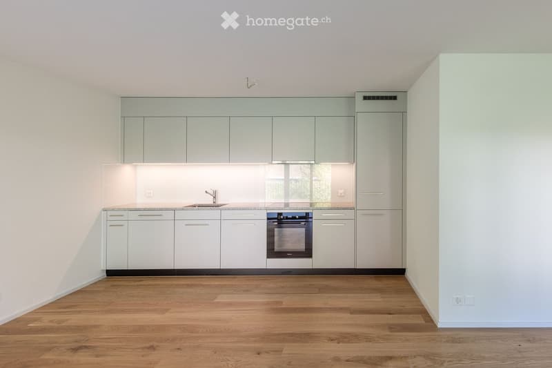 Modern kitchen with light grey cabinets, a stainless steel oven, a sink with a faucet, and a light wooden floor.