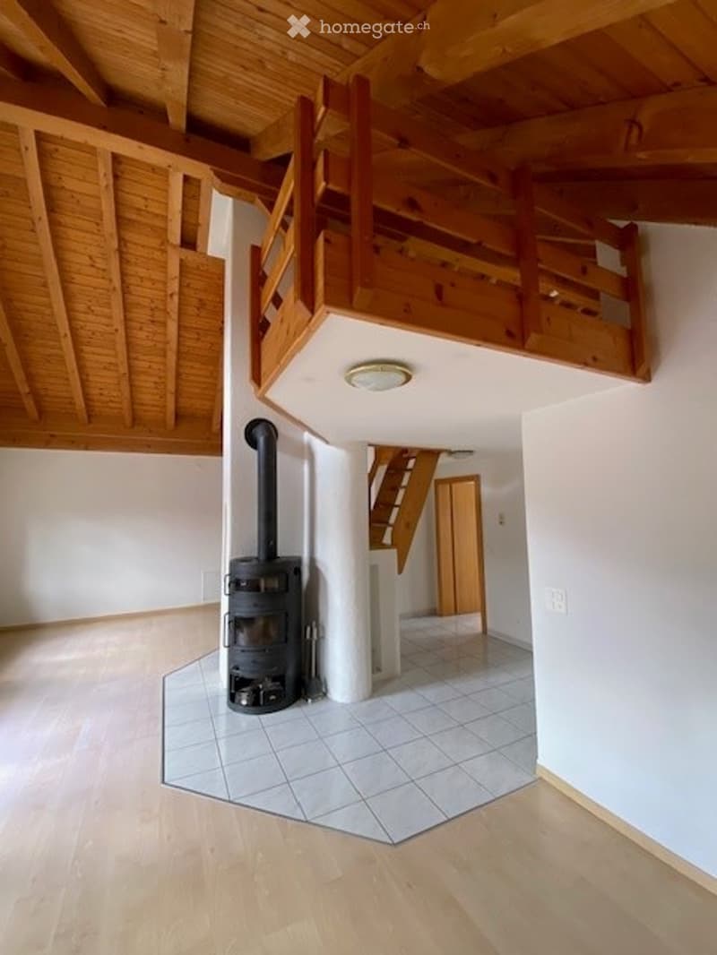 Bright hallway with wooden floors, white walls, and a visible staircase leading to an upper level. A wood-burning stove is placed near the wall.