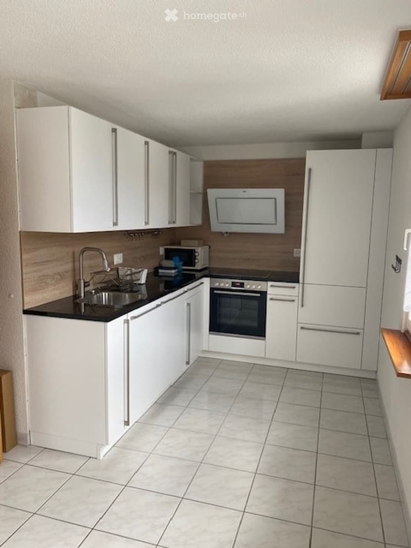 Modern kitchen with white cabinets, black countertops, and stainless steel appliances including a sink, microwave, oven, and refrigerator.
