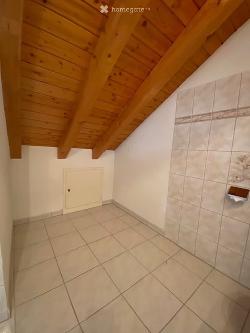 Empty bathroom with tiled floor and walls, wooden slanted ceiling, and a closed white door.