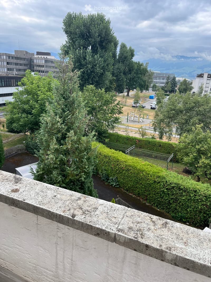 Balcony overlooking a park area with trees, playground, and buildings in the background.
