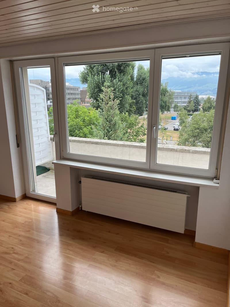Empty room with wooden flooring, large windows, radiator, and sliding glass door leading to a balcony.