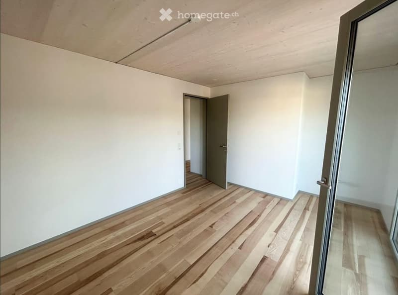Empty room with wooden flooring, white walls, and a single door leading to another space.