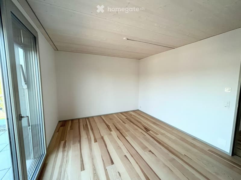 Empty room with light wooden flooring, white walls, and a large glass door leading outside.