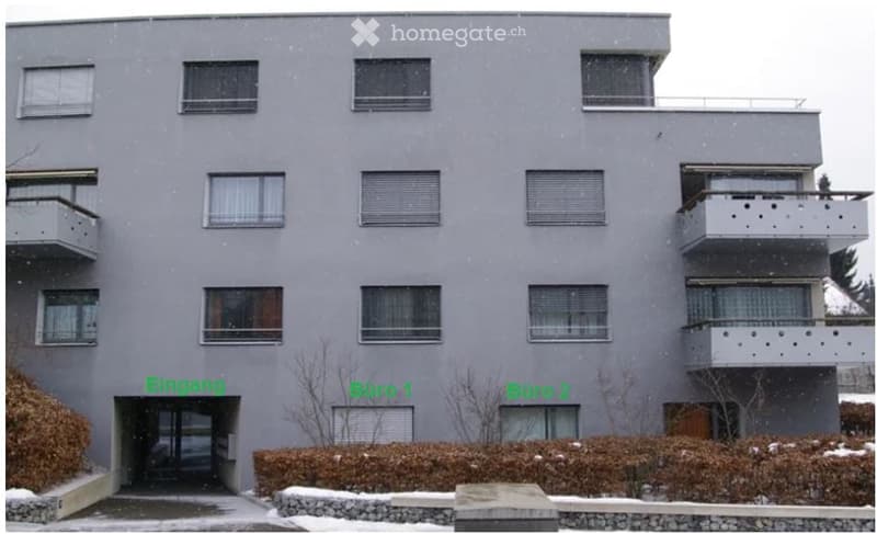 Modern multi-story apartment building with grey facade, multiple balconies, and snow-covered surroundings.