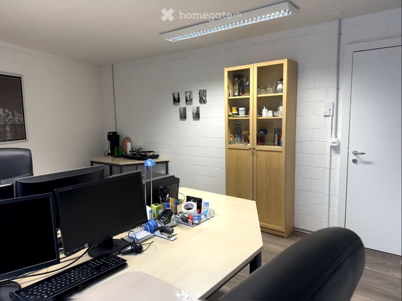 Office space with a wooden table, multiple computer screens, chairs, a wooden cupboard, and a coffee machine.