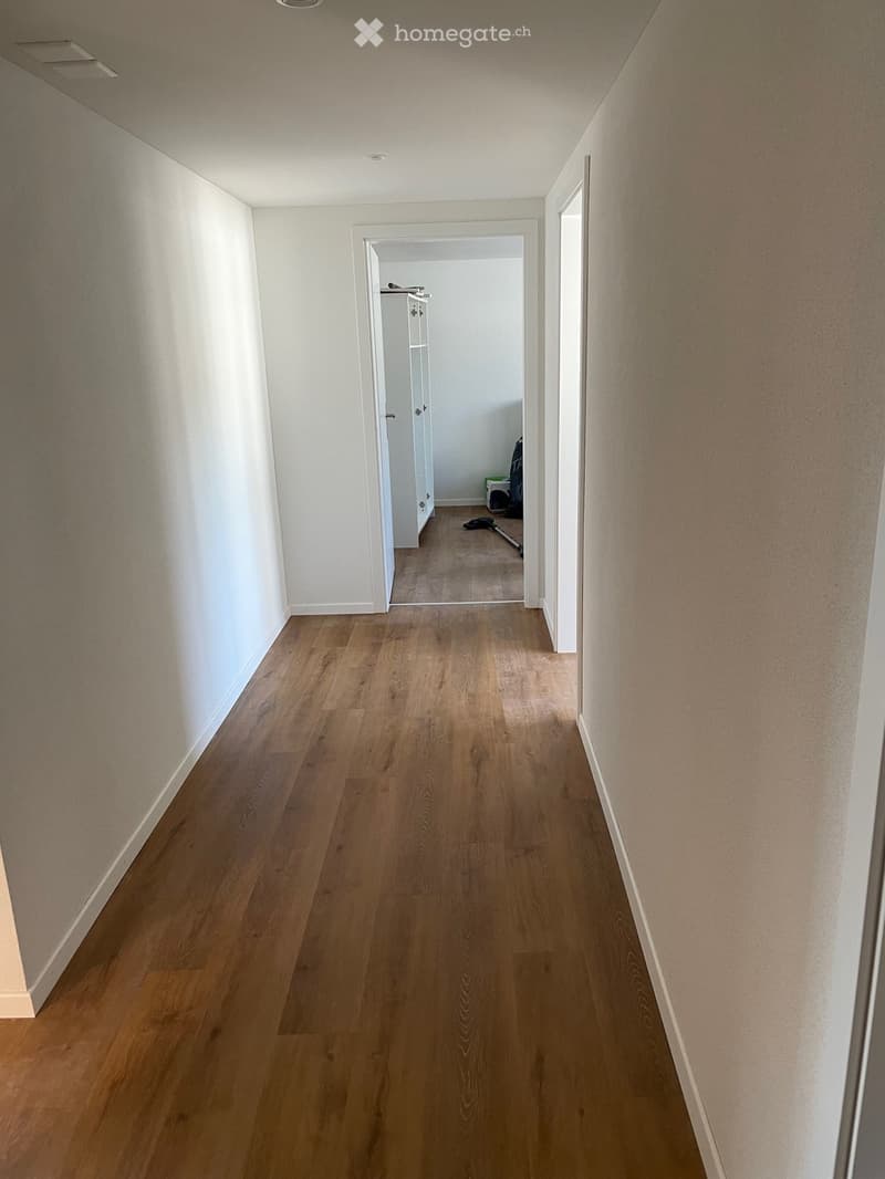 Empty hallway with wooden flooring and white walls, leading to an open doorway.