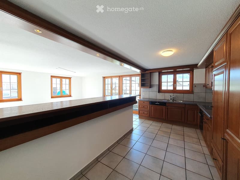 Empty kitchen with wooden cabinets, tiled floor, and large windows. No furniture or appliances are present.