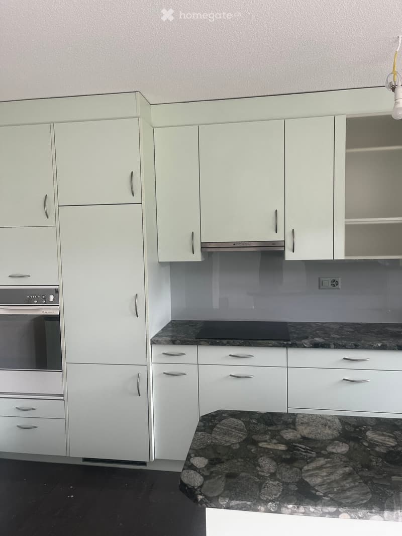 Modern kitchen with white cabinets, stainless steel appliances, granite countertop, and dark stone floor.
