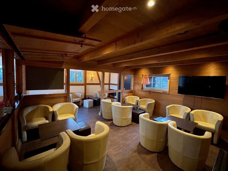 white leather chairs around tables, wooden floor, large wooden beams, televisions on wall, lamps