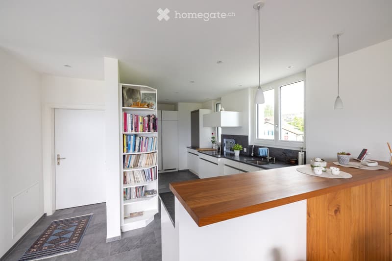 Modern kitchen with white cabinets, wooden island, bookshelf, sink, and various small items on the island.