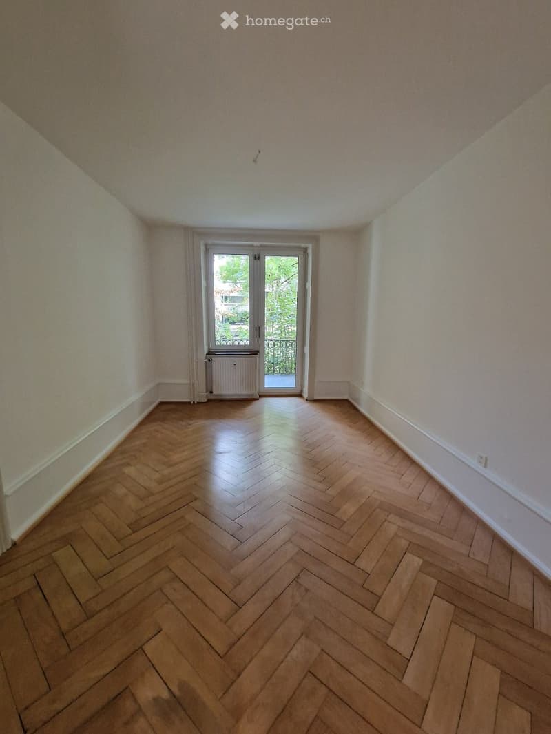 Empty room with wooden herringbone flooring, light-colored walls, and a door leading to a balcony or outdoor area.