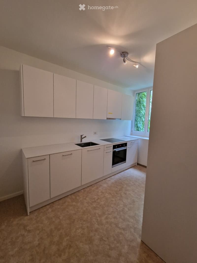 Modern kitchen with white cabinets, a sink, a faucet, and an oven. The space is well-lit with recessed lighting and has a large window letting in natural light.