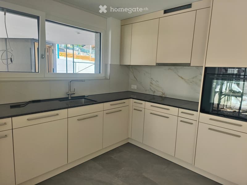 Modern kitchen with light-colored cabinets, black countertops, and a marble backsplash. Features a sink with a modern faucet and an integrated oven.