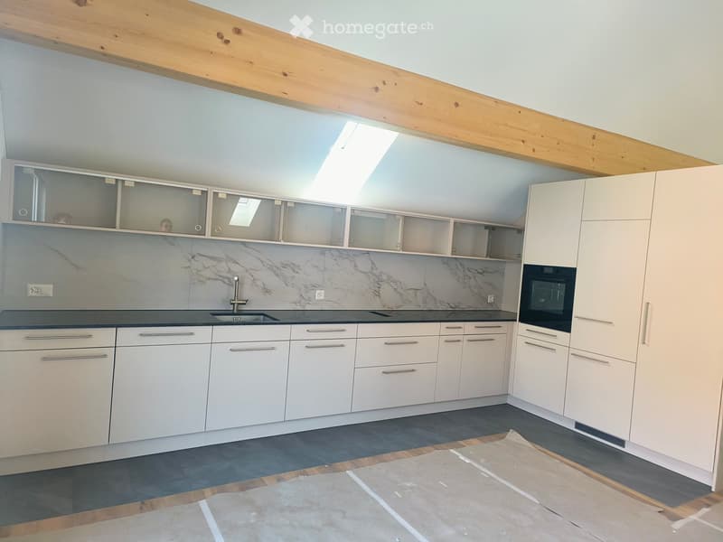 Modern kitchen with white cabinets, marble backsplash, and stainless steel sink and oven. Exposed wooden beams on the ceiling and a skylight provide natural light.