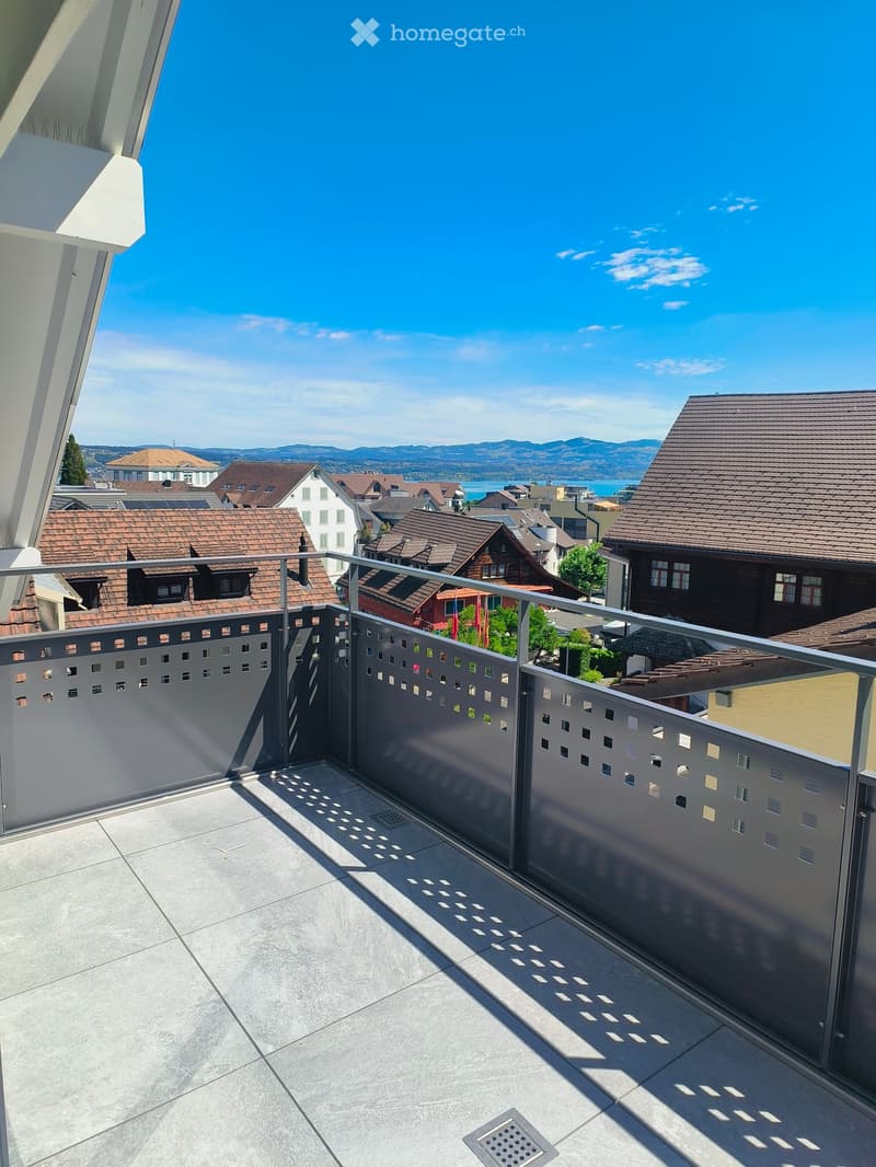Balcony with modern metal railing, tiled floor, and scenic view of a town with houses and mountains in the background.