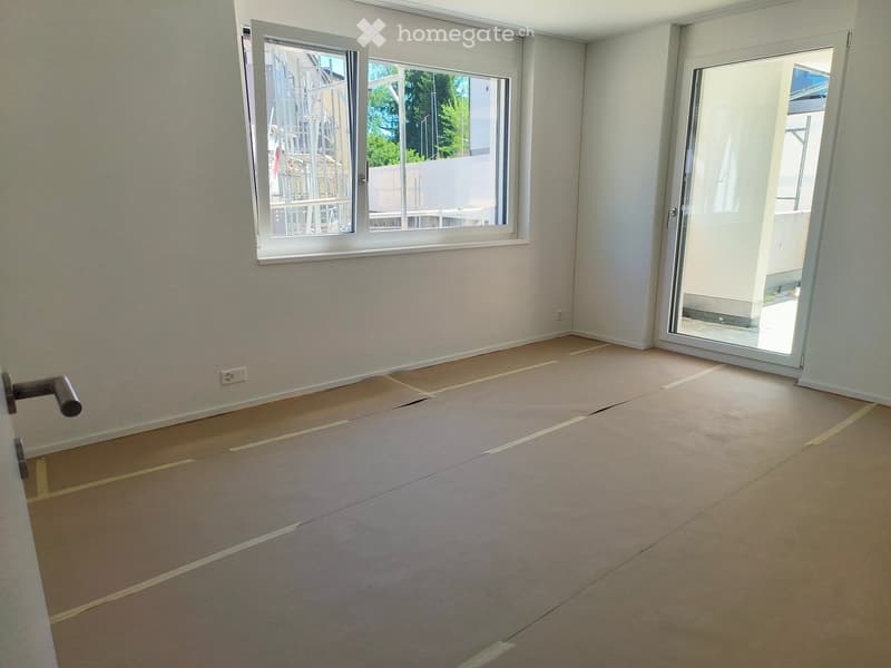 Empty room with bare walls, wooden floor, and large windows. No furniture or equipment present.