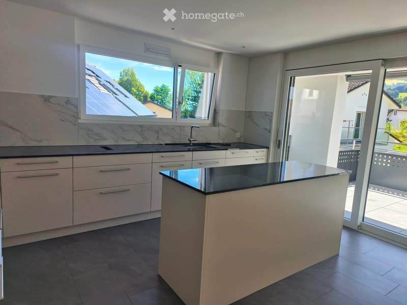 Modern kitchen with white cabinets, black countertops, a central island, and large windows overlooking a sunny outdoor area.