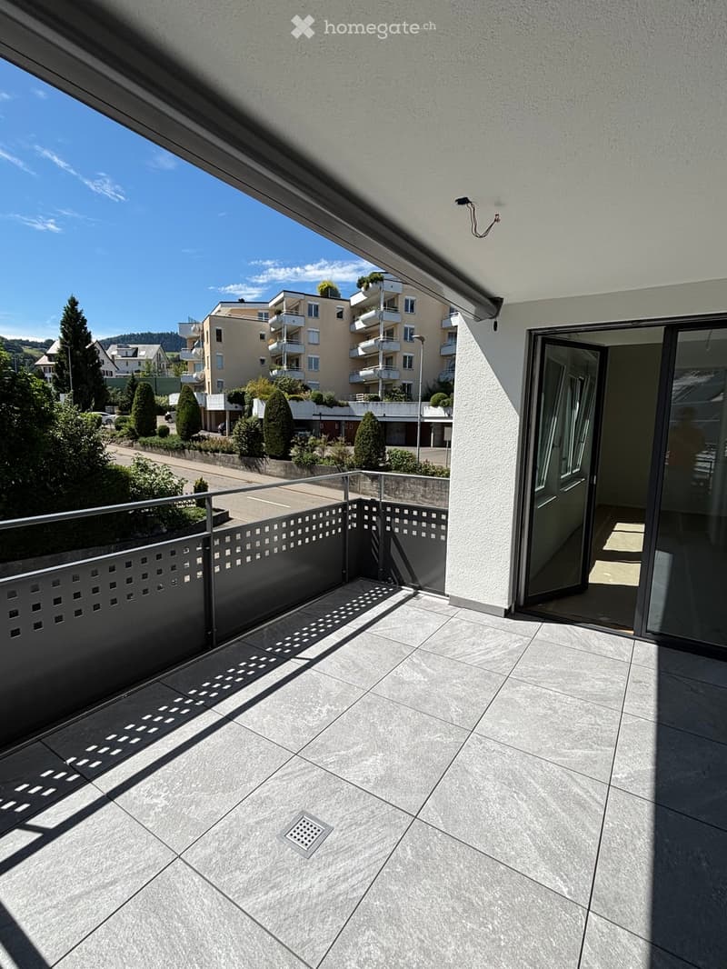 Balcony with tiled floor, metal railing, and a view of a residential area with buildings and greenery.