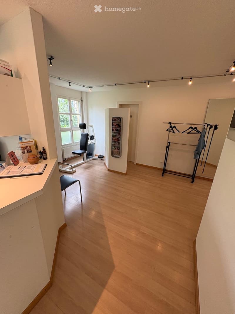 A well-lit room with wooden flooring, a desk with a chair, a mirror, a clothing rack, and various small items on a counter.
