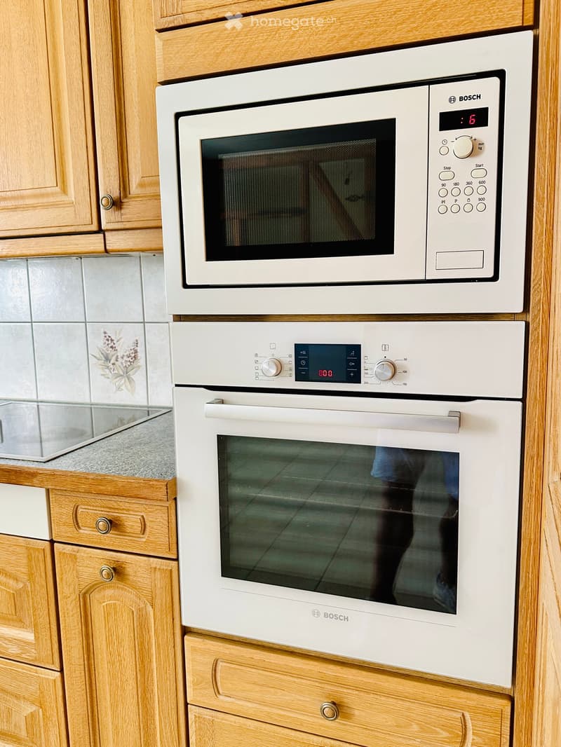 White Bosch microwave, oven, and dishwasher mounted in a kitchen with wooden cabinets and tiled backsplash.