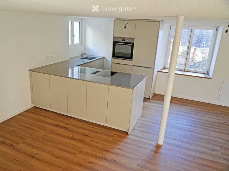 Modern kitchen with light-colored cabinets, a central island with a stainless steel countertop, and built-in appliances including an oven and sink.