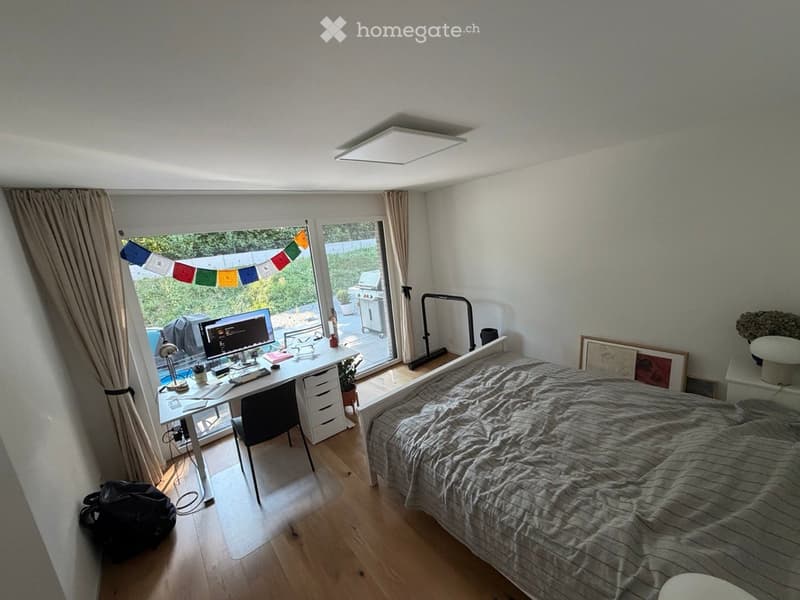 Cozy bedroom with a bed, desk, and chair. Large window with a view of the garden, decorated with colorful flags.