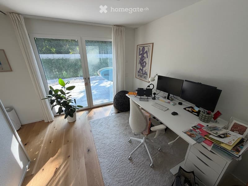 Bright, modern workspace with a large desk, dual monitors, ergonomic chair, and a comfortable beanie chair near the sliding glass door leading to a patio.