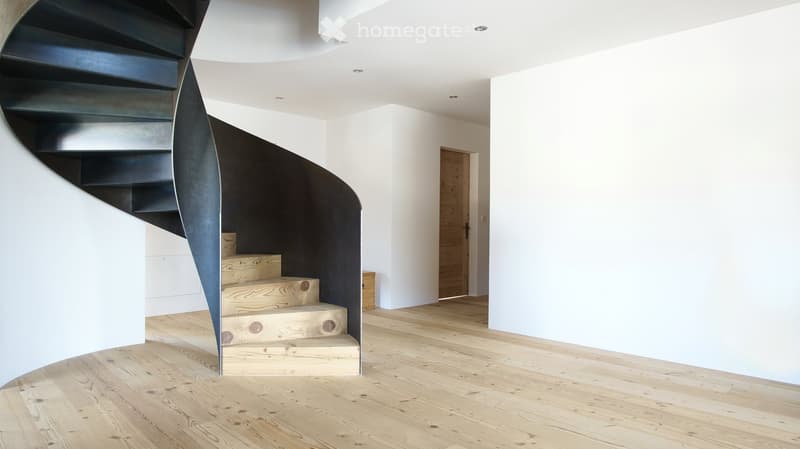 Modern hallway with a wooden floor, white walls, and a unique black spiral staircase leading upwards.