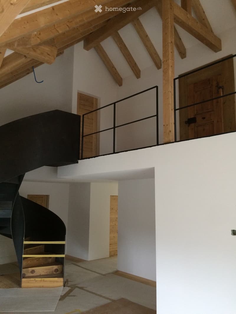 Empty room with exposed wooden beams, white walls, and a staircase leading to an upper level. The space is clean and unfurnished, with a modern, minimalist design.