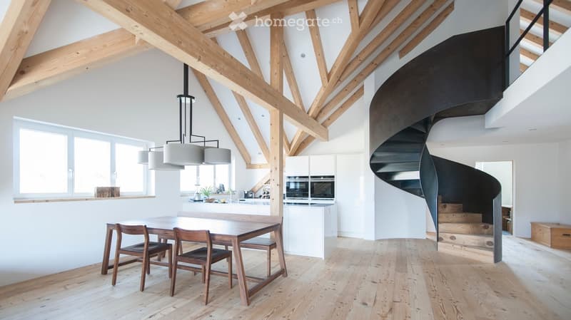 Open-plan dining and kitchen area with exposed wooden beams, modern pendant lights, and a sleek black spiral staircase leading to an upper level.