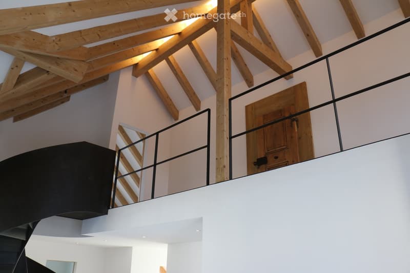 Modern interior with exposed wooden beams and a sleek black metal railing leading to an upper level.