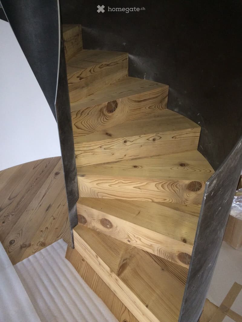Wooden staircase with polished steps and handrails, leading upwards in a modern interior setting.