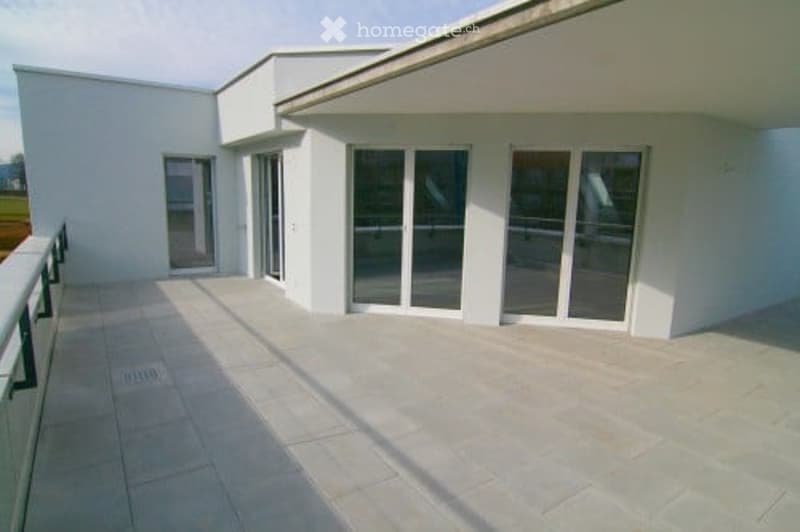 Modern balcony with large glass doors leading to a white building, tiled floor, and metal railing.
