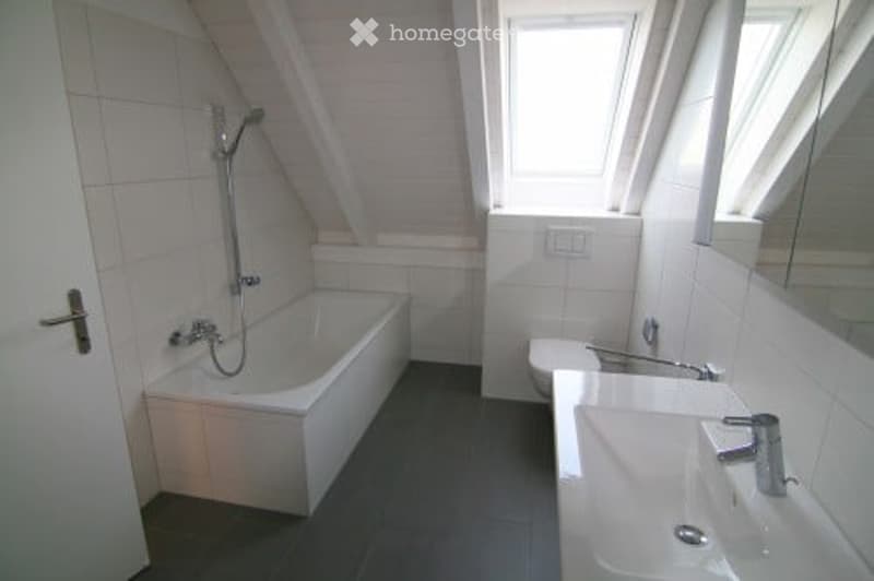 Modern bathroom with a bathtub, sink, and showerhead. The room features white tiles and a window with blinds.