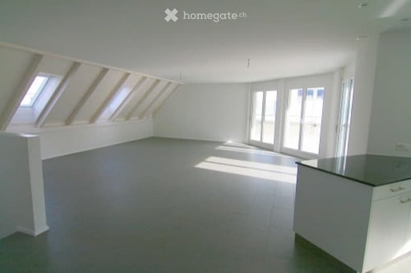 Bright, open room with large windows and skylights, featuring a kitchen area with a counter and cabinets.