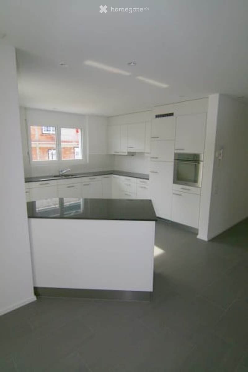 Modern kitchen with white cabinets, black countertops, and a central island. Features a sink, faucet, and built-in oven.