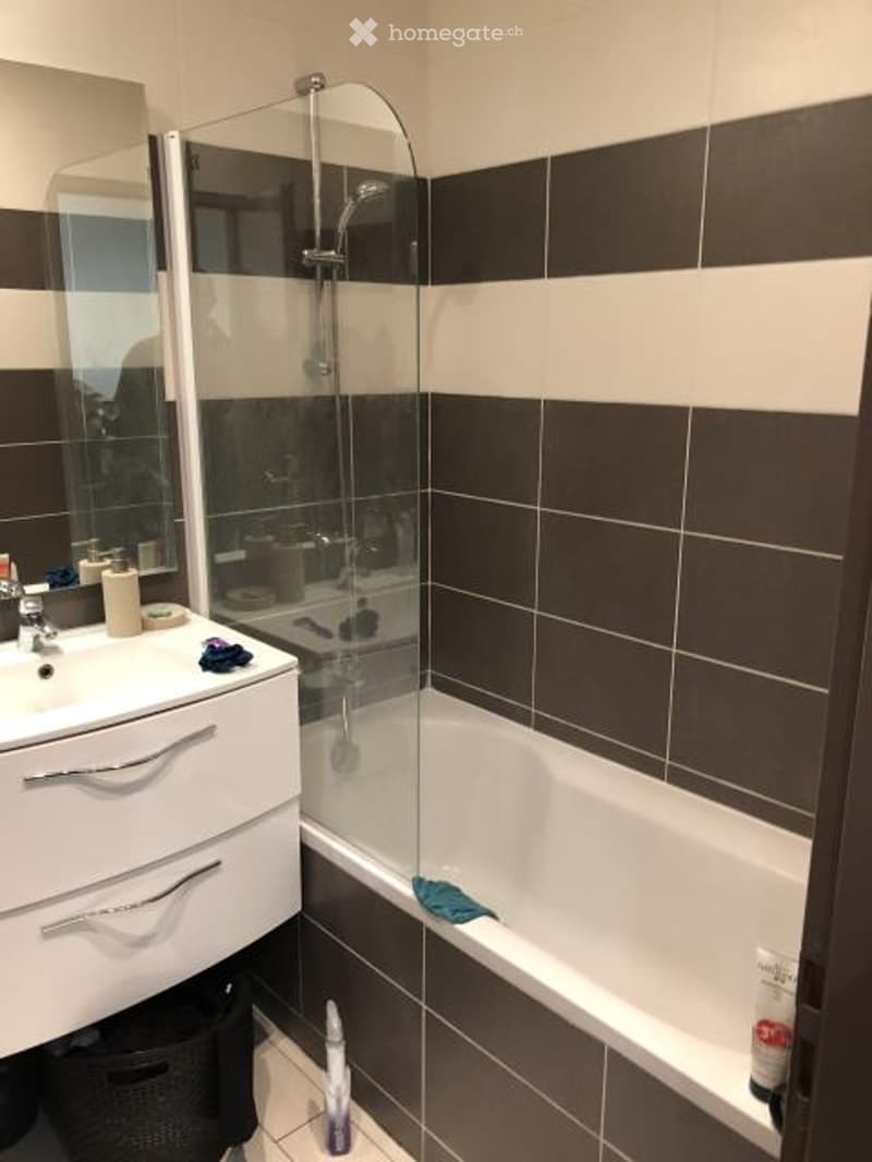 Modern bathroom with white sink, mirror, bathtub, and glass shower stall. Dark brown tiles on walls, white tiles on floor.