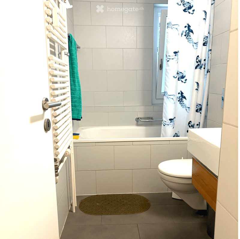 Modern bathroom with white tiles, bathtub, toilet, sink, towel, and a decorative shower curtain.