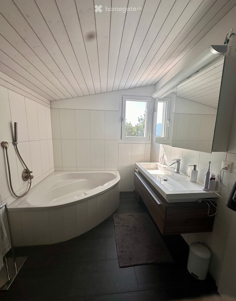 Modern bathroom with a white bathtub, double sink, large mirror, and a window providing natural light.