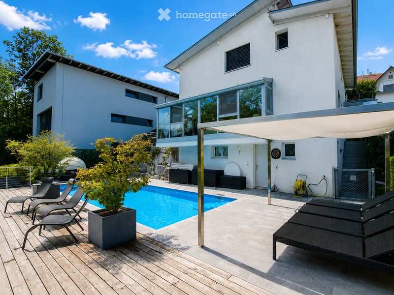 Modern two-story house with a swimming pool, lounge chairs, and a covered patio area.