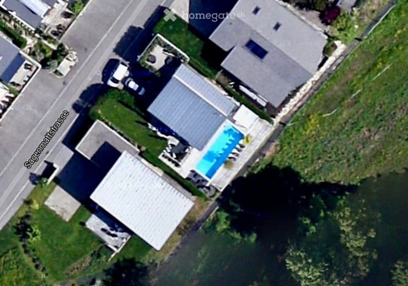 Aerial view of a residential property with a swimming pool, surrounded by greenery and neighboring houses.