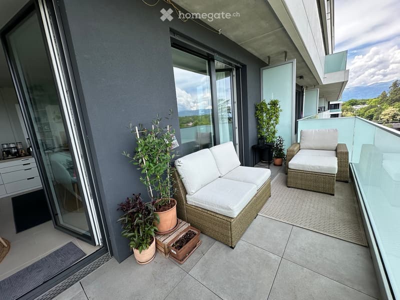 Balcony with a wicker sofa, matching chair, and potted plants, overlooking a scenic view.
